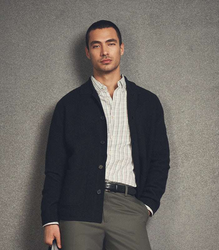 Man wearing a dark cardigan over a striped shirt against a gray background