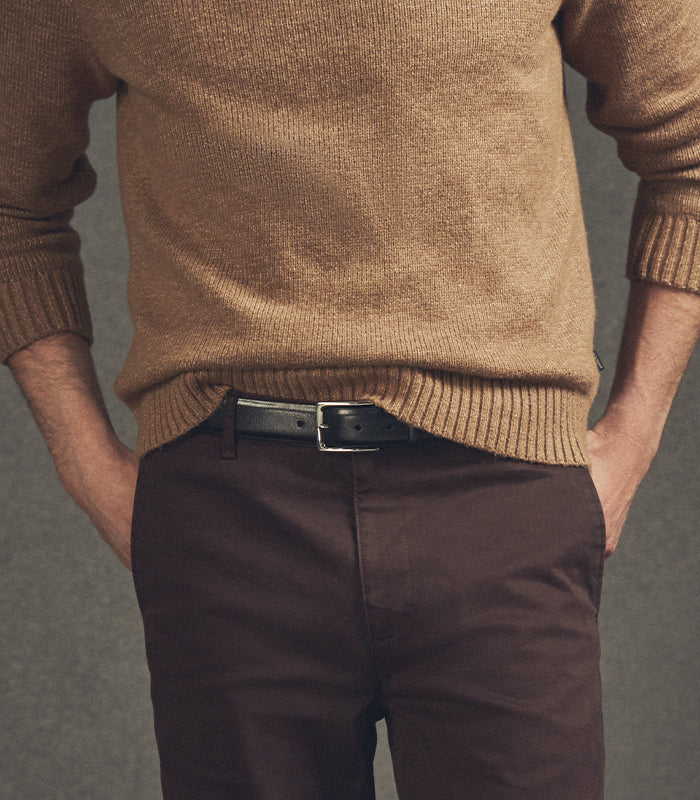 Person wearing a brown sweater and dark pants against a gray background