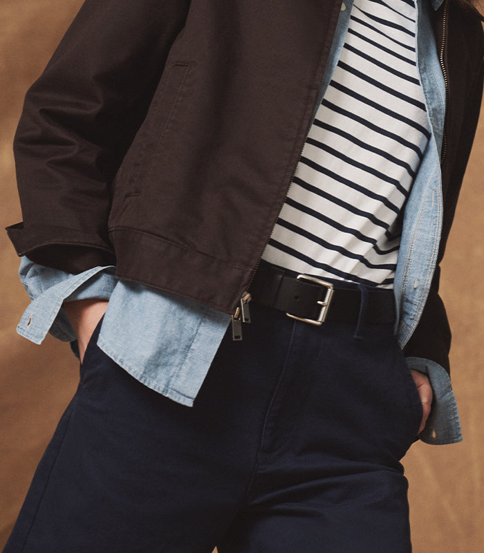 Person wearing a dark jacket, striped shirt, and jeans with a brown background