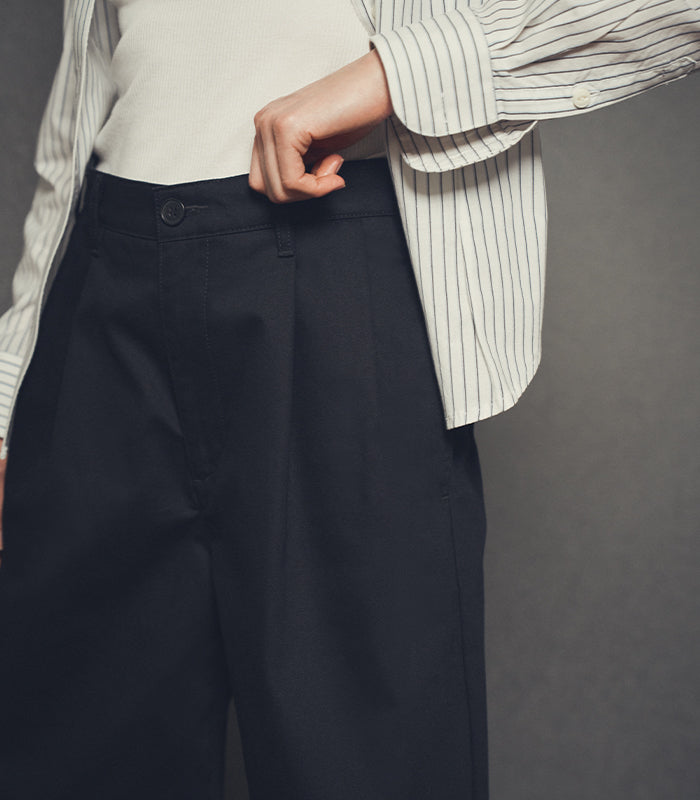 Person wearing a white shirt with a striped pattern and dark pants against a gray background